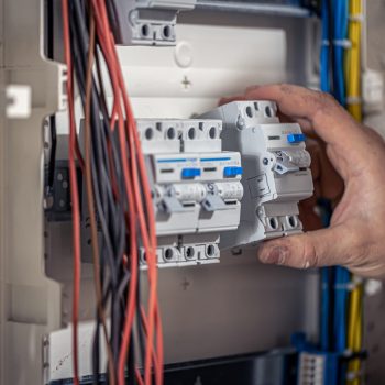 A male electrician works in a switchboard with an electrical connecting cable, connects the equipment with tools.